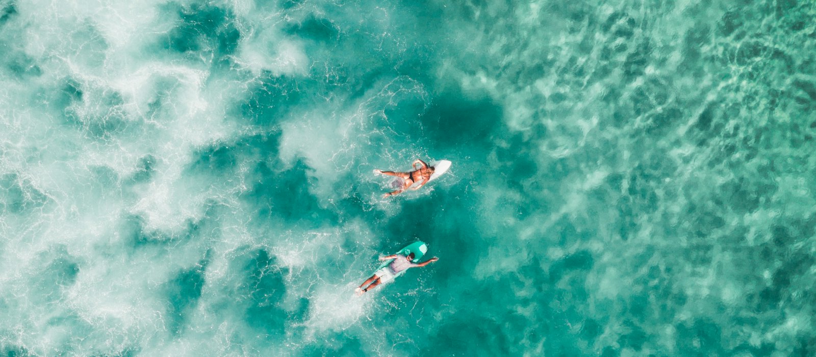 Zwei Surfer von oben im türkisen Wasser